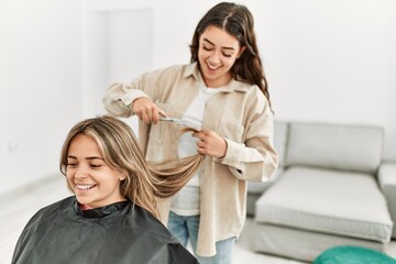 Young woman cutting hair to her girlfriend at home.