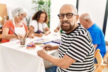 Group of middle age draw students sitting on the table drawing at art studio. Man smiling happy looking to the camera.