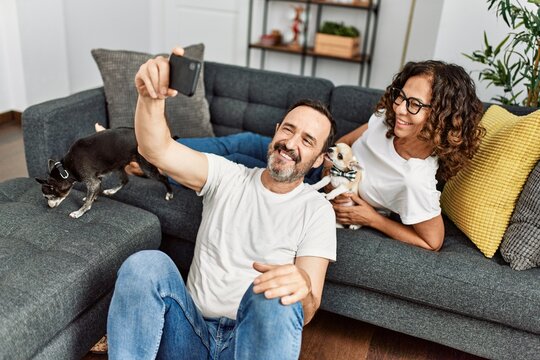 Middle age hispanic couple smiling happy and making selfie by the smartphone. Sitting on the sofa with dogs at home.