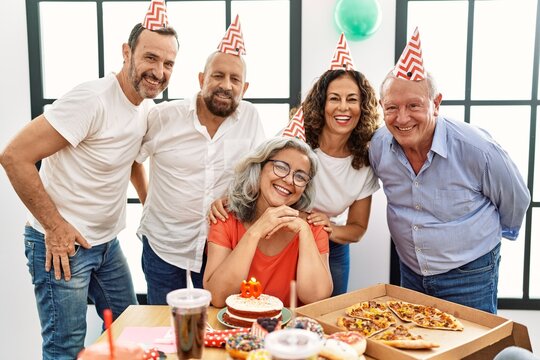 Group of middle age friends celebrate birthday looking at the camera at home.