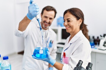 Middle age man and woman partners wearing scientist uniform using pipette and test tube at laboratory