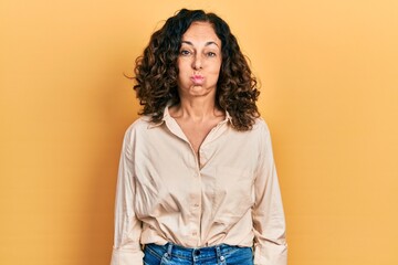 Middle age hispanic woman wearing casual clothes puffing cheeks with funny face. mouth inflated with air, crazy expression. - obrazy, fototapety, plakaty