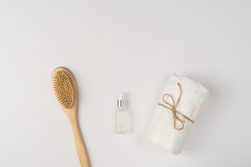 Flat lay, a set of bath products. Eco-friendly wooden brush, clean fresh towel and oil serum for face and body on a white background.