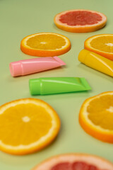 Cosmetics, hand and body skin care with vitamin C, small colorful tubes and juicy oranges and grapefruits on a light green background.