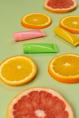 Cosmetics, hand and body skin care with vitamin C, small colorful tubes and juicy oranges and grapefruits on a light green background.
