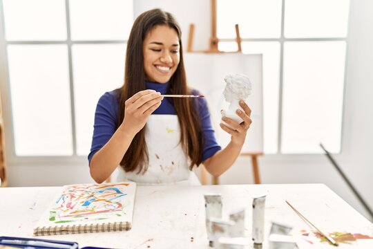 Young latin woman smiling confident painting bust sculpture at art studio
