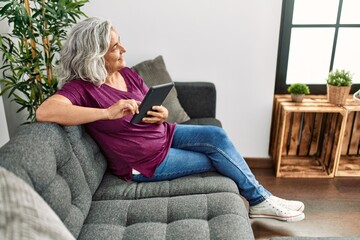 Fototapeta na wymiar Middle age grey-haired woman using touchpad sitting on the sofa at home.