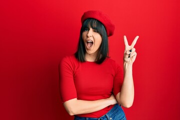 Young hispanic woman wearing french look with beret smiling with happy face winking at the camera...