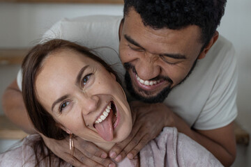 Black man and caucasian woman couple in white clothes, fool around. Close-up guy strangles girl by the neck as a joke. Joy and happiness concept.