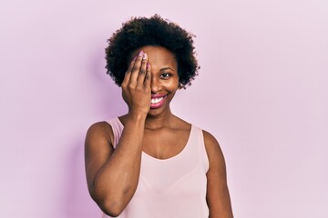 Fototapeta na wymiar Young african american woman wearing casual sleeveless t shirt covering one eye with hand, confident smile on face and surprise emotion.
