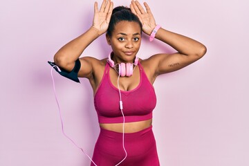 Young african american girl wearing gym clothes and using headphones doing bunny ears gesture with hands palms looking cynical and skeptical. easter rabbit concept.