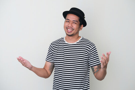 Tattooed Asian man smiling friendly with both arms open showing welcoming gesture