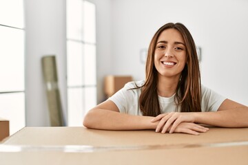 Obraz premium Young hispanic woman smiling confident leaning on package at new home