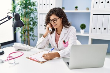 Obraz premium Young latin woman wearing doctor uniform talking on the telephone at clinic