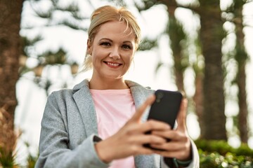 Young blonde businesswoman smiling happy using smartphone at the city.