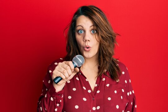 Young caucasian woman singing song using microphone scared and amazed with open mouth for surprise, disbelief face