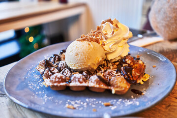  Plate of waffle with chocolate sauce and ice cream on wooden surface