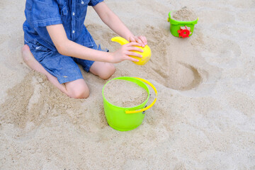 child, boy of 6-8 years plays in summer with sand on seashore, in sandbox, on playground, concept of development of fine motor skills, build sand castles, summer vacation, fun on beach