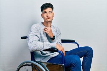 Fototapeta na wymiar Young hispanic man sitting on wheelchair thinking concentrated about doubt with finger on chin and looking up wondering