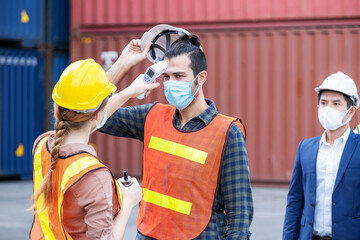 Female engineer worker scanning to check temperature of staff before entering to the container construction site by using digital thermometer. Wearing hygiene face mask. New normal concept