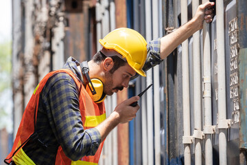 American engineer worker wearing helmet and vest standing at shipping container terminal. Inspector...