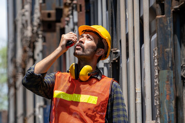 American engineer worker wearing helmet and vest standing at shipping container terminal. Inspector...