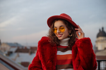 Happy smiling fashionable woman wearing trendy orange glasses, hat, faux fur coat, turtleneck sweater, big earrings. Outdoor close up winter fashion, lifestyle portrait. Copy, empty space for text