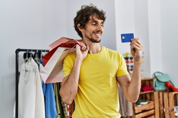 Young hispanic man holding shopping bags and credit card at clothing store