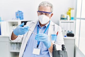 Middle age grey-haired man wearing scientist uniform using syringe at laboratory