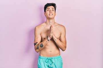 Young hispanic man wearing swimwear shirtless begging and praying with hands together with hope...