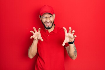 Hispanic man with beard wearing delivery uniform and cap smiling funny doing claw gesture as cat,...