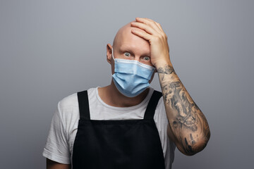 Surprised and frightened bald chef or butcher holding his head. On gray background.