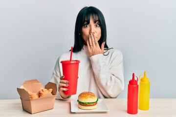 Young brunette woman with bangs eating a tasty classic burger with ketchup and mustard covering...