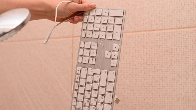 Close-up woman washes white computer keyboard under running water.