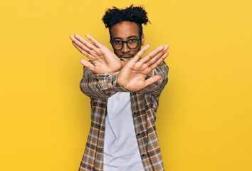 Young african american man with beard wearing casual clothes and glasses rejection expression crossing arms and palms doing negative sign, angry face - obrazy, fototapety, plakaty