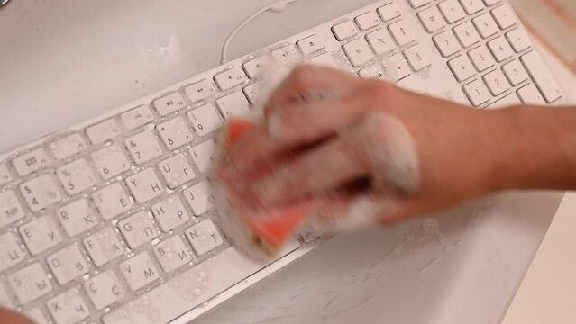 Woman washing white computer keyboard with a sponge with foam.