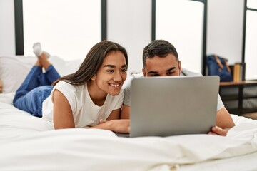 Young latin couple smiling happy using laptop lying on the bed.