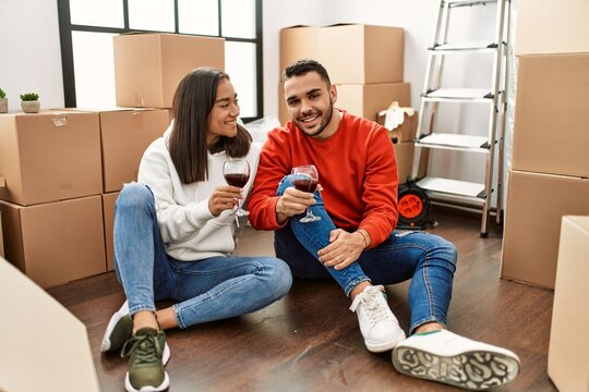 Young latin couple smiling happy toasting with red wine at new home