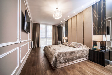 Large double bed in the bedroom. The room has been renovated in Baroque style in brown and beige tones. Plaster panel with patterns in the corners