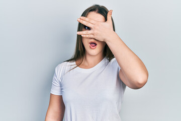 Young hispanic girl wearing casual white t shirt peeking in shock covering face and eyes with hand, looking through fingers afraid