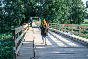 a woman tourist with a backpack walks along a wooden bridge in the countryside.