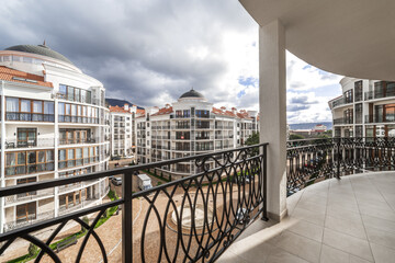 Fototapeta na wymiar A wide curved balcony of a multi-storey building with metal black wrought iron railings with patterns. The balcony offers a view of the houses of the residential complex, mountains and clouds