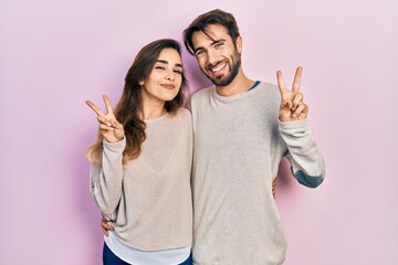 Young hispanic couple wearing casual clothes smiling looking to the camera showing fingers doing...