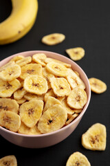 Homemade Banana Chips in a Pink Bowl on a black background, side view.