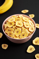 Homemade Banana Chips in a Pink Bowl on a black surface, low angle view.