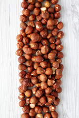 Unshelled Hazelnut in a Bowl on a white wooden surface, top view. Flat lay, overhead, from above.