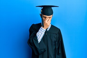 Middle age hispanic man wearing graduation cap and ceremony robe tired rubbing nose and eyes feeling fatigue and headache. stress and frustration concept.