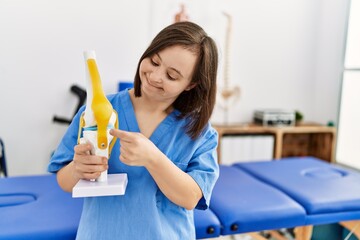 Brunette woman with down syndrome working holding anatomical knee at physiotherapy clinic