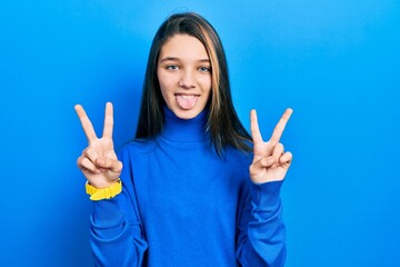Young brunette girl wearing turtleneck sweater smiling with tongue out showing fingers of both...
