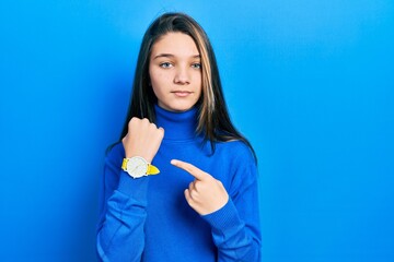 Young brunette girl wearing turtleneck sweater in hurry pointing to watch time, impatience, looking at the camera with relaxed expression